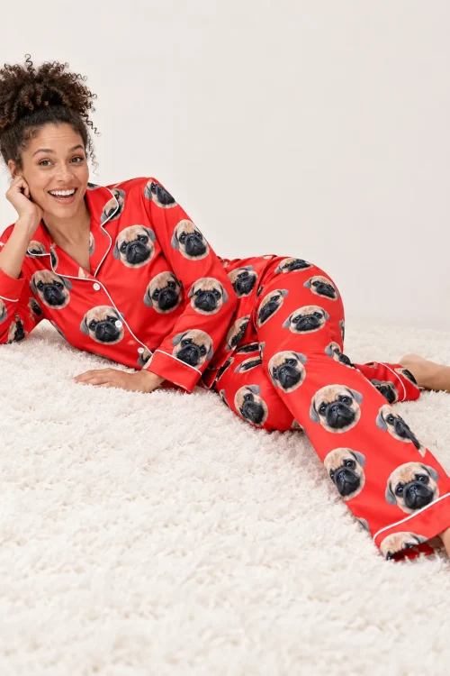 Laughing woman lying on a white shaggy rug in red satin pajamas printed with pug faces