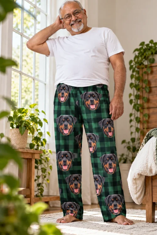 Older man in glasses in a sunny bedroom, wearing green plaid pajama pants printed with Rottweiler faces