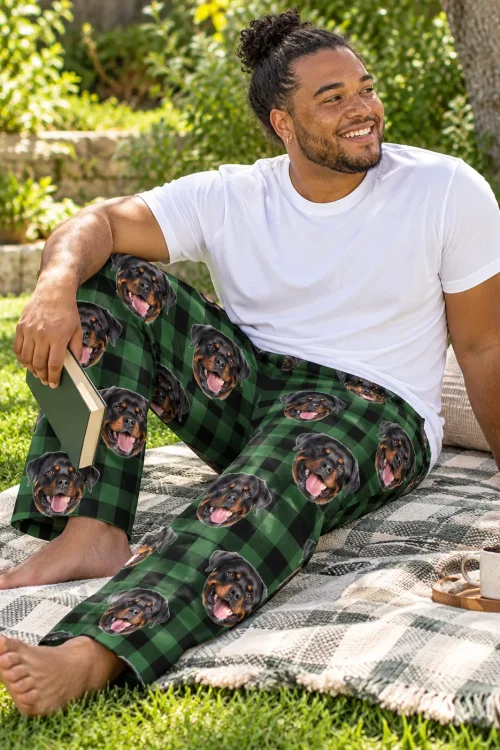 Man reading on a picnic blanket in the garden in green buffalo plaid pajama pants with Rottweiler faces