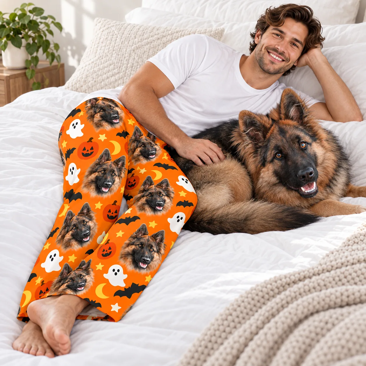 Pet face pajamas: man relaxing on a bed with his German shepherd, wearing orange Halloween pajama pants with its face