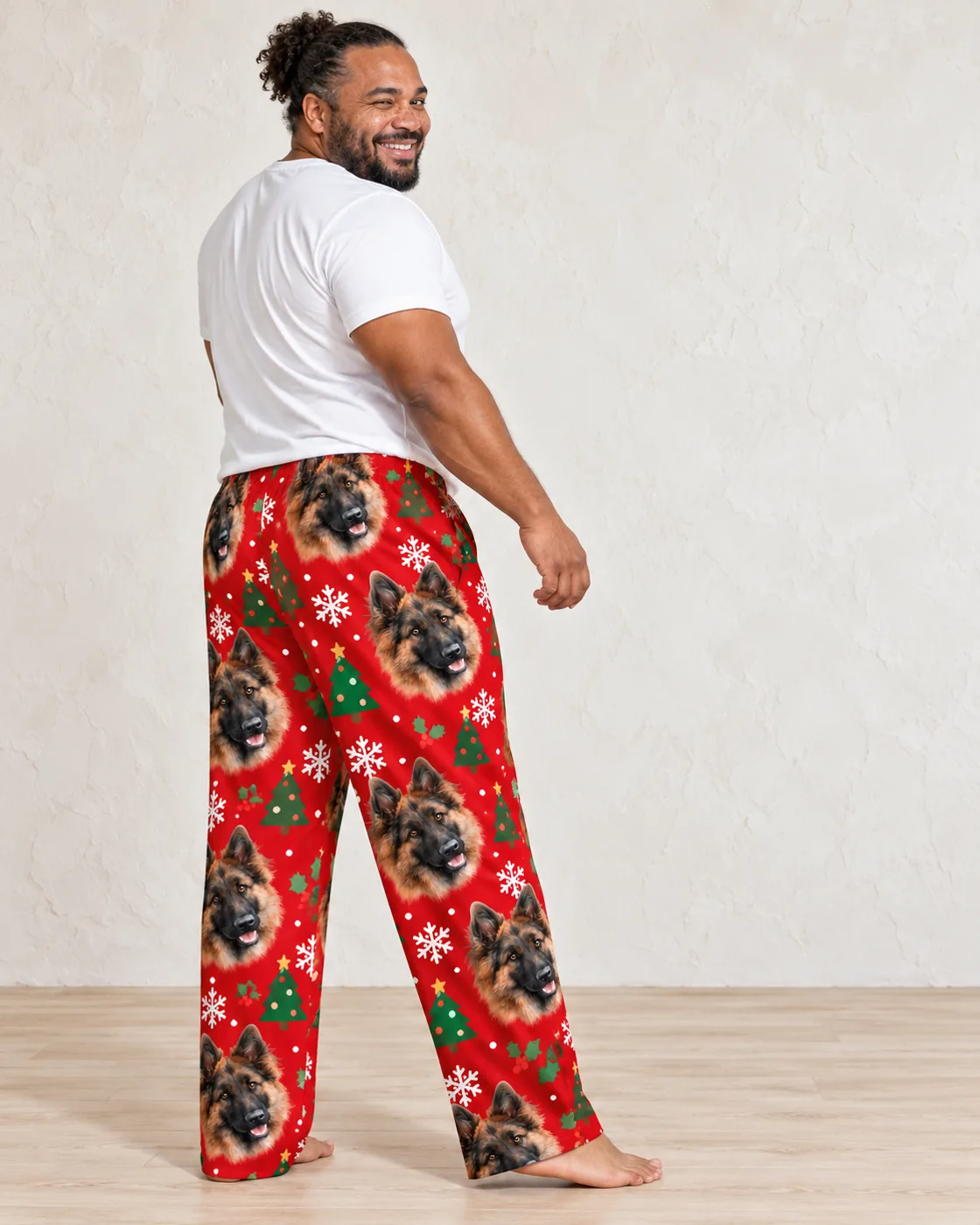 Pet face pajamas: man in a white tee wearing red mens Christmas pajama pants with German Shepherd faces, trees and snowflakes