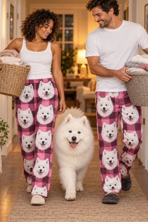 Couple carrying laundry baskets down a warm hallway with their samoyed, both in pink plaid samoyed pajama pants