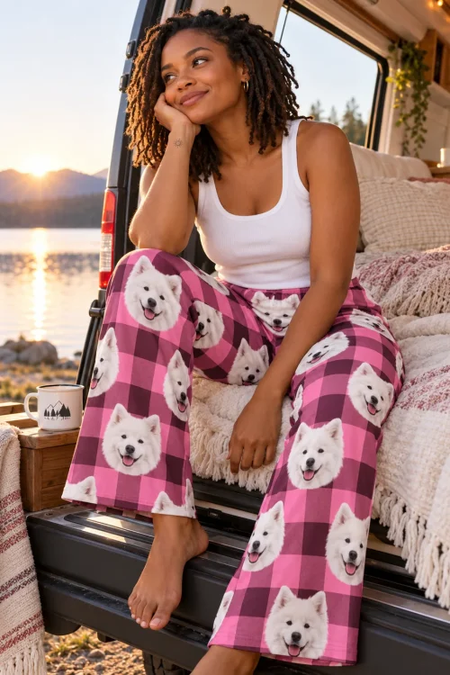 Woman with short locs sitting on a camper van tailgate at a lake sunset, in pink plaid samoyed pajamas