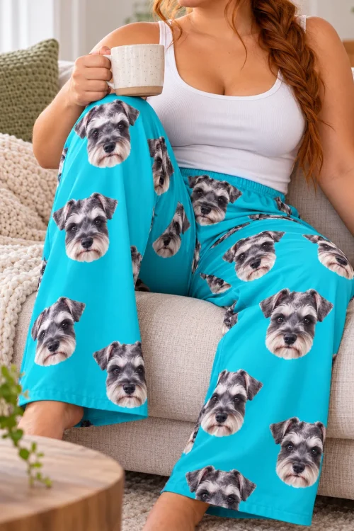 Seated woman on a cream sofa holding a speckled mug, wearing teal pajama pants printed with schnauzer faces