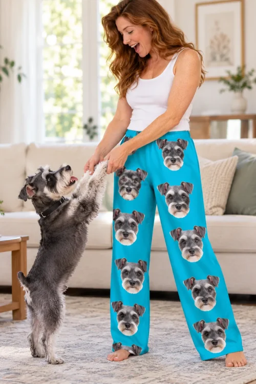 Red-haired woman holding the front paws of her salt-and-pepper schnauzer standing up, in teal schnauzer pajama pants