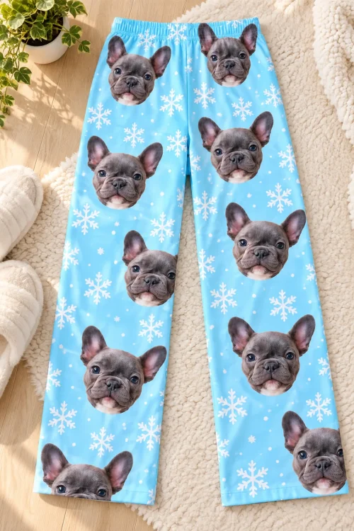 Snowflake pajama pants with French bulldog faces laid flat on a rug next to white slippers