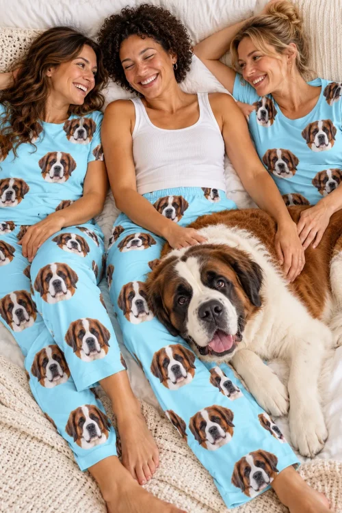 Three friends laughing on a bed with a giant St Bernard, matching light blue pajamas printed with dog faces