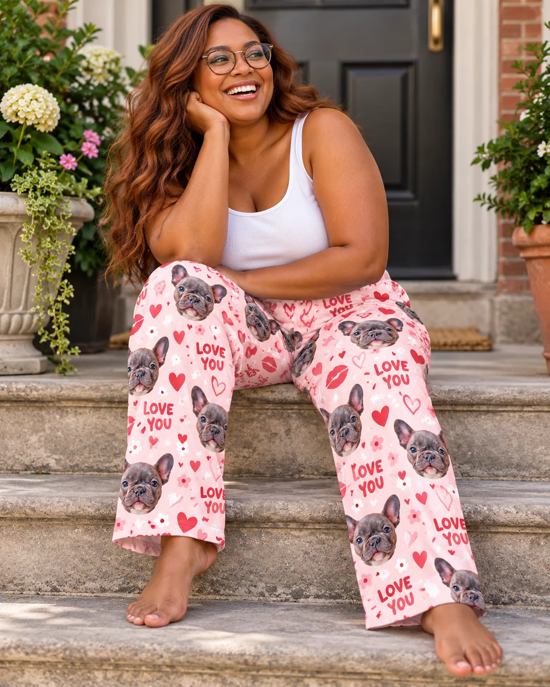 Woman in glasses on stone front steps in valentine pajama pants with love-you hearts and French bulldog faces