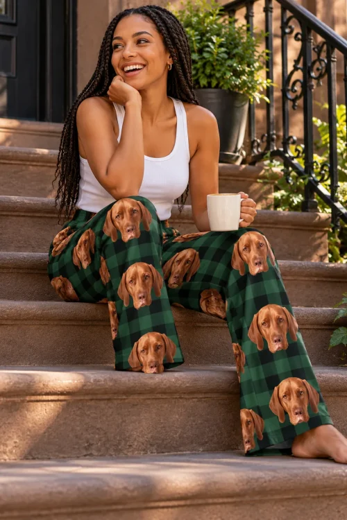 Woman with long braids laughing on brownstone steps with a coffee mug, in green plaid vizsla pajama pants