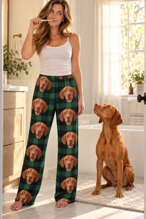 Woman brushing her teeth in a sunny bathroom in vizsla pajama pants, her golden-rust vizsla sitting beside her