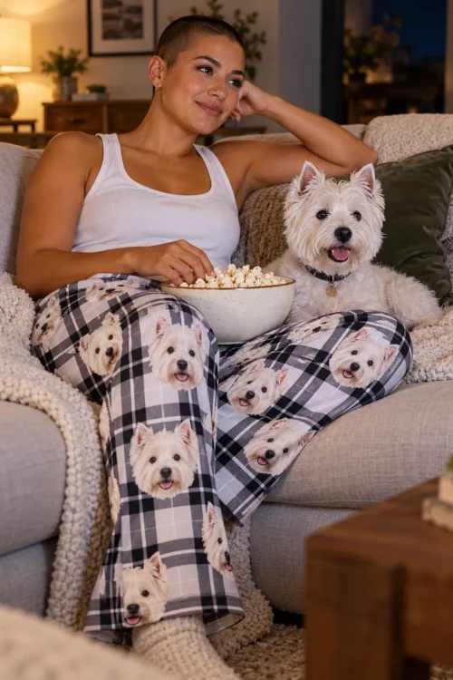 Woman on a couch with a bowl of popcorn and her white Westie, wearing plaid Westie pajamas on movie night
