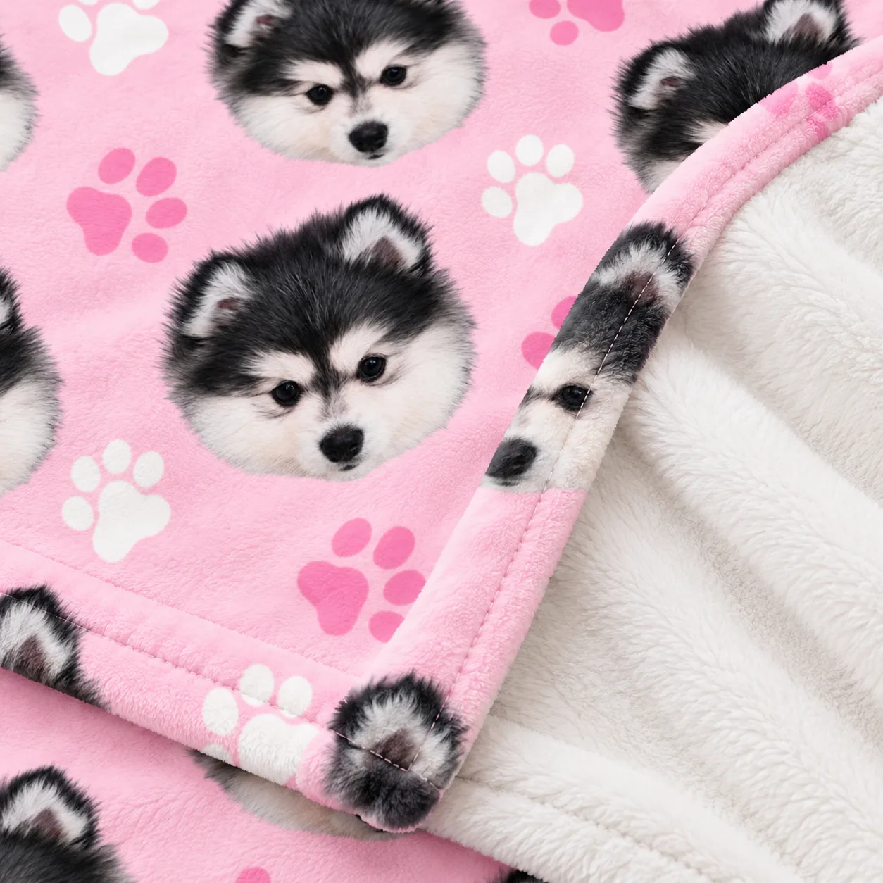 Close-up of a pink minky blanket printed with husky puppy faces, plush back and stitched edge
