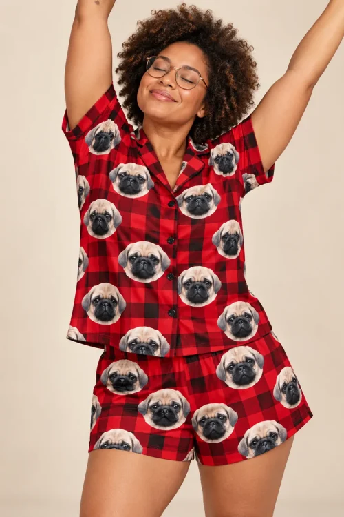 Woman in glasses stretching both arms up in a red buffalo plaid pajama set printed with pug faces