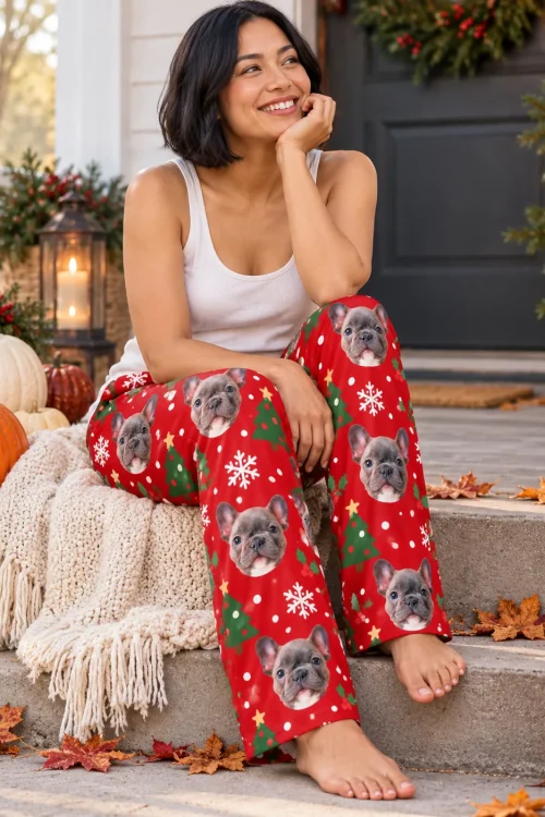 Woman on porch steps with pumpkins and a wreath in red Christmas pajama pants with French bulldog faces