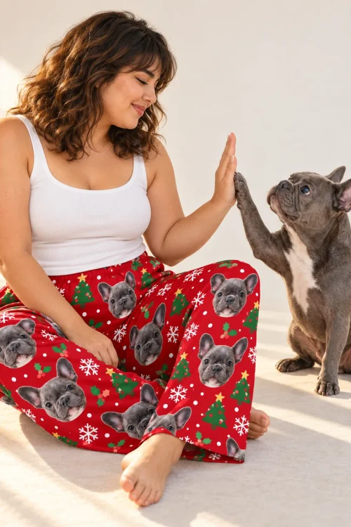 Woman high-fiving her French bulldog, wearing Christmas pajama pants printed with its face