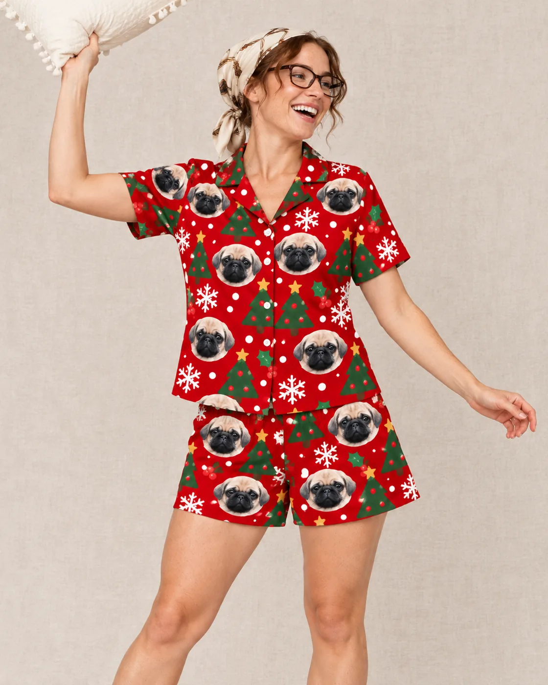 Women's Christmas pajamas: woman in a red Christmas short set printed with pug faces, laughing with a pillow