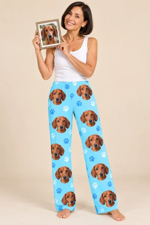 Smiling woman in a white tank holding a framed dachshund photo, wearing light blue paws women's dachshund pajamas