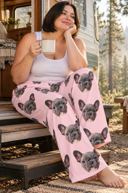 Woman with a mug on a camper trailer step in pink pajama pants printed with French bulldog faces
