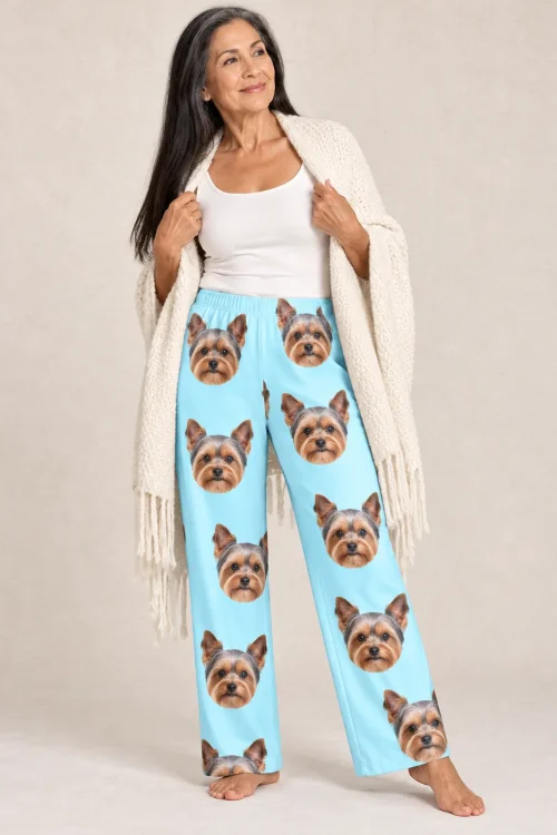 Woman in a cream knit shawl and light blue women's Yorkie pajama pants covered in Yorkie faces, beige studio