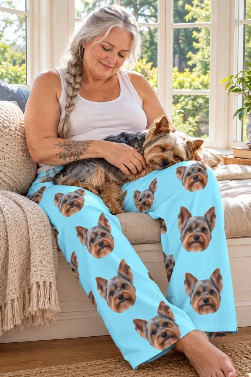 Woman on a sunny window seat in light blue Yorkie pajama pants, her sleeping Yorkie curled up in her lap