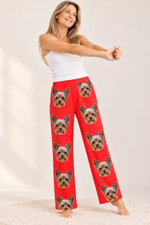 Smiling woman stretching in red Yorkie pajama pants printed with steel-blue and tan Yorkie faces, cream studio