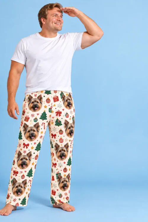Man shading his eyes in cream Christmas Yorkshire terrier pajama pants with trees and gifts, sky-blue backdrop