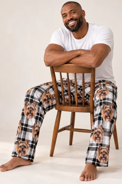 Smiling man straddling a wooden chair in white plaid Yorkshire terrier pajama pants, light studio backdrop