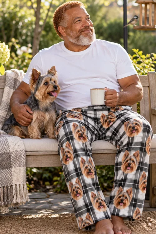 Bearded man with coffee on a garden bench hugging his Yorkie, in white plaid Yorkshire terrier pajama pants